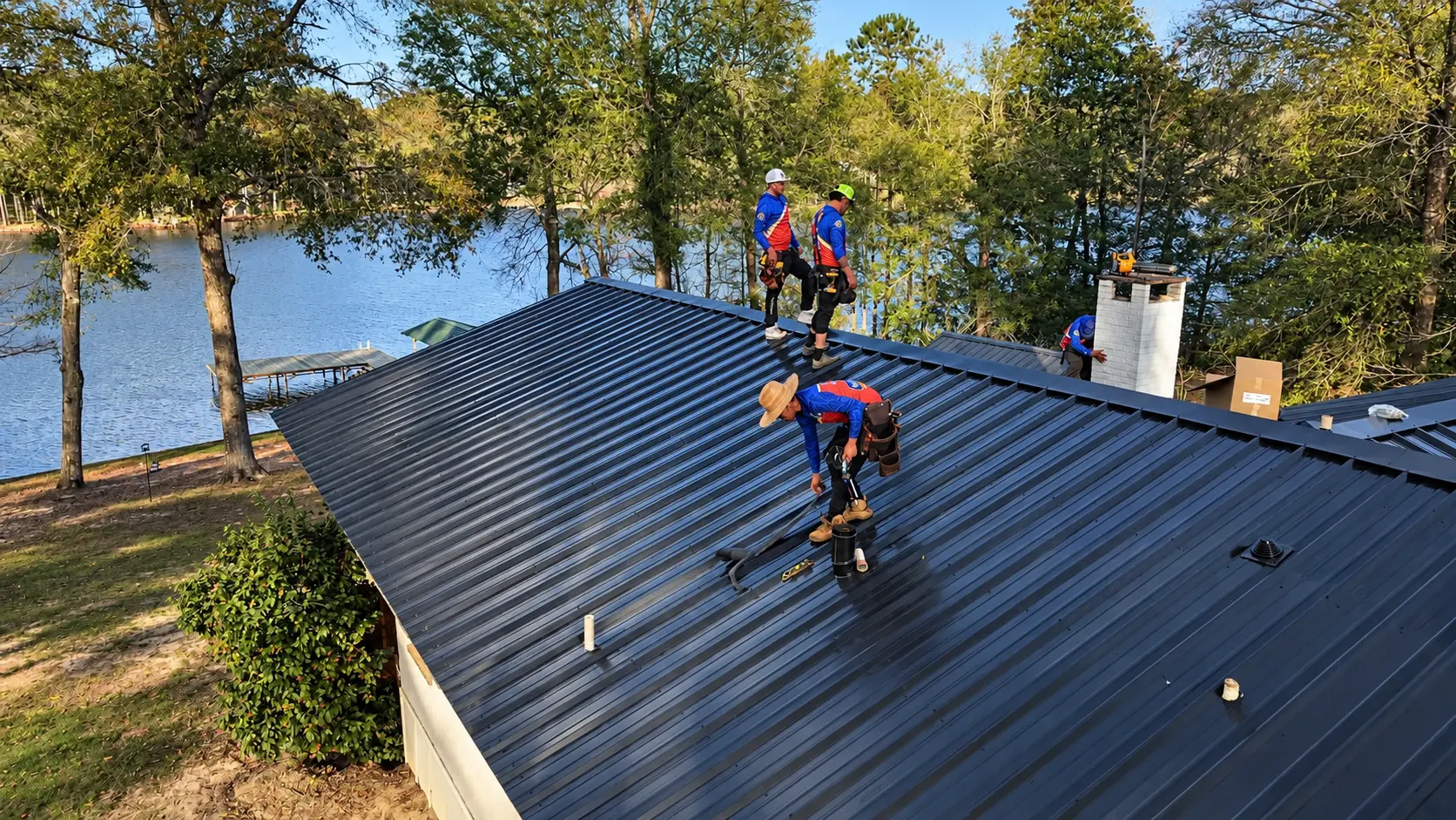 Roof Ryders crew working on a metal roof by the lake